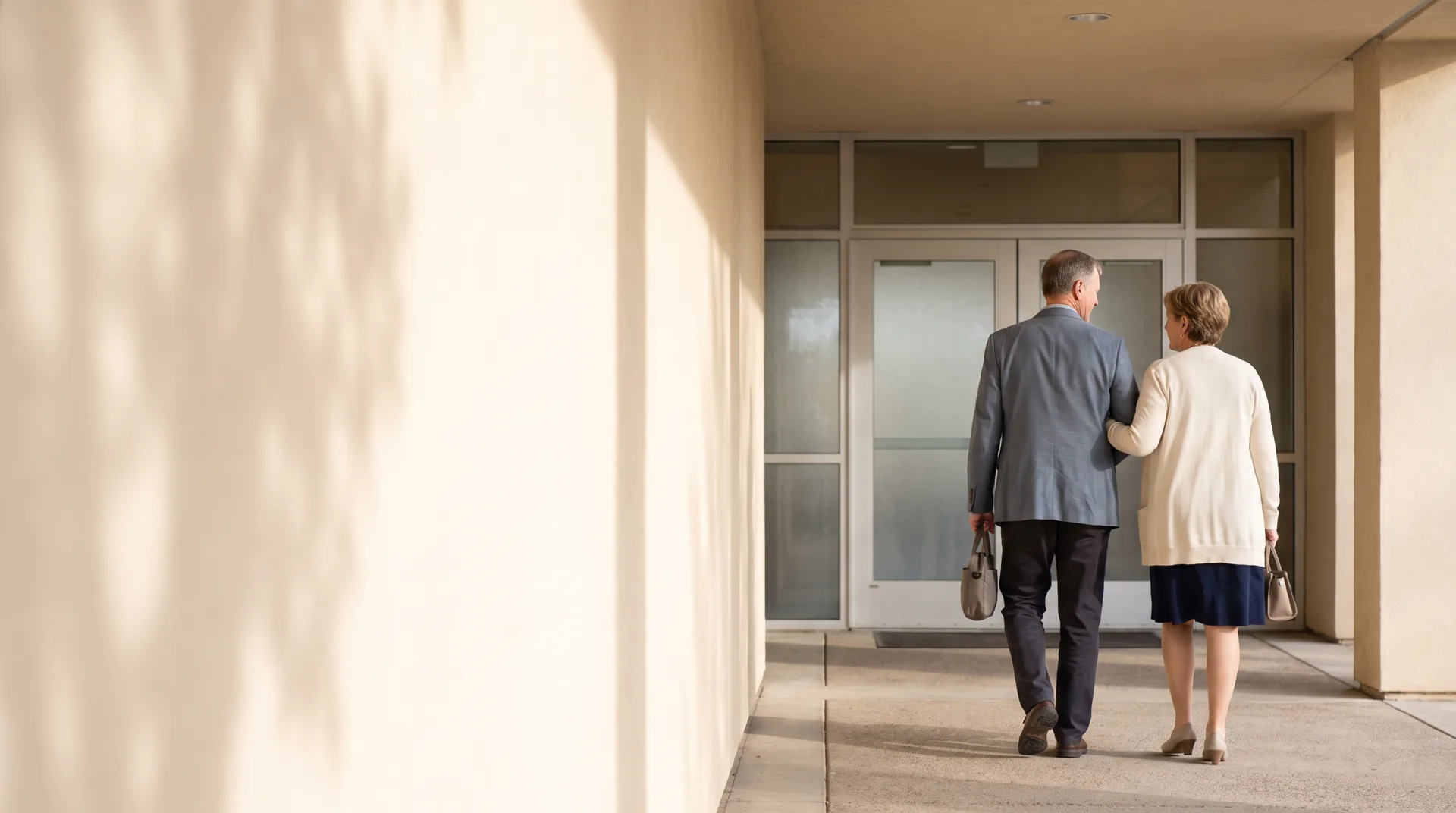Two adults walking together toward the entrance of a healthcare facility in warm daylight.